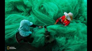 two-women-become-lost-in-the-fabric-of-a-fishing-net-in-vinh-hy-ninh-thuan-vietnam-they-are-sewingthe-net-for-a-new-fishing-season-while-the